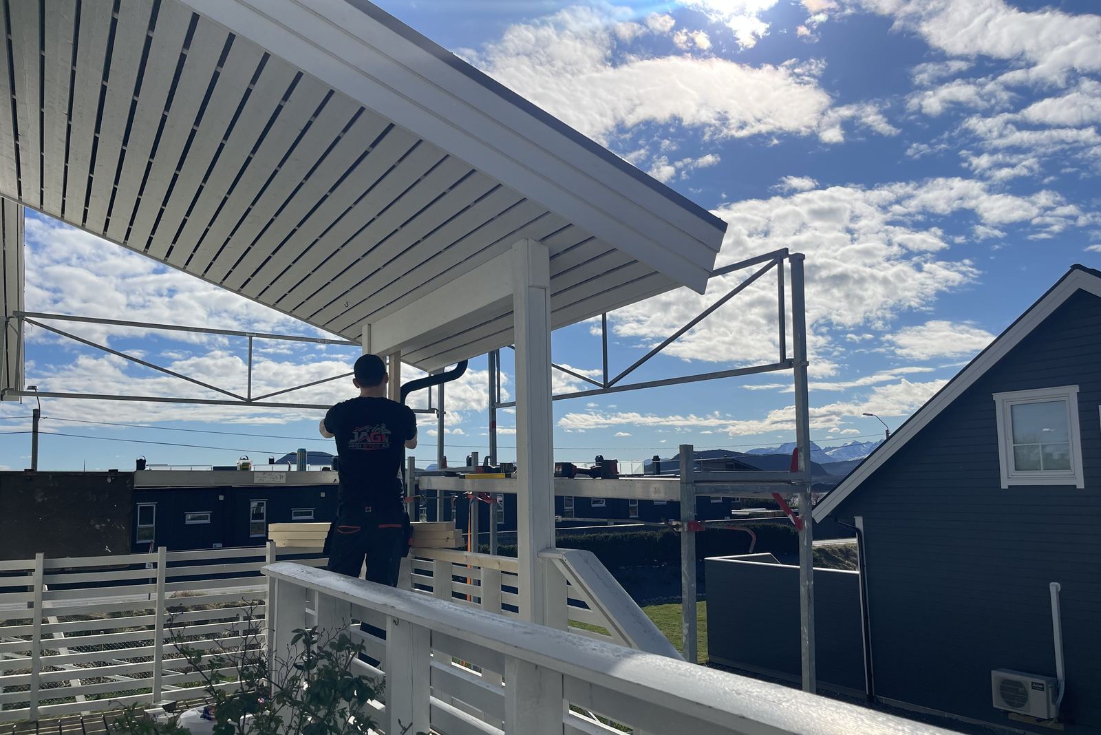 Jacob bygger tak over en terrasse, med rekkverk og blå himmel